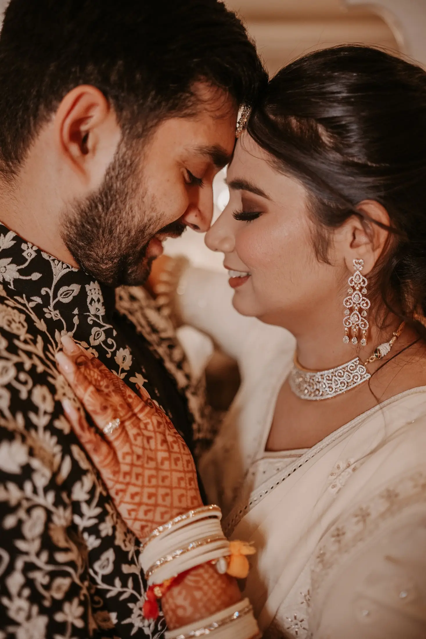 Bride and groom sharing a tender moment, the bride wearing mehendi and a diamond necklace