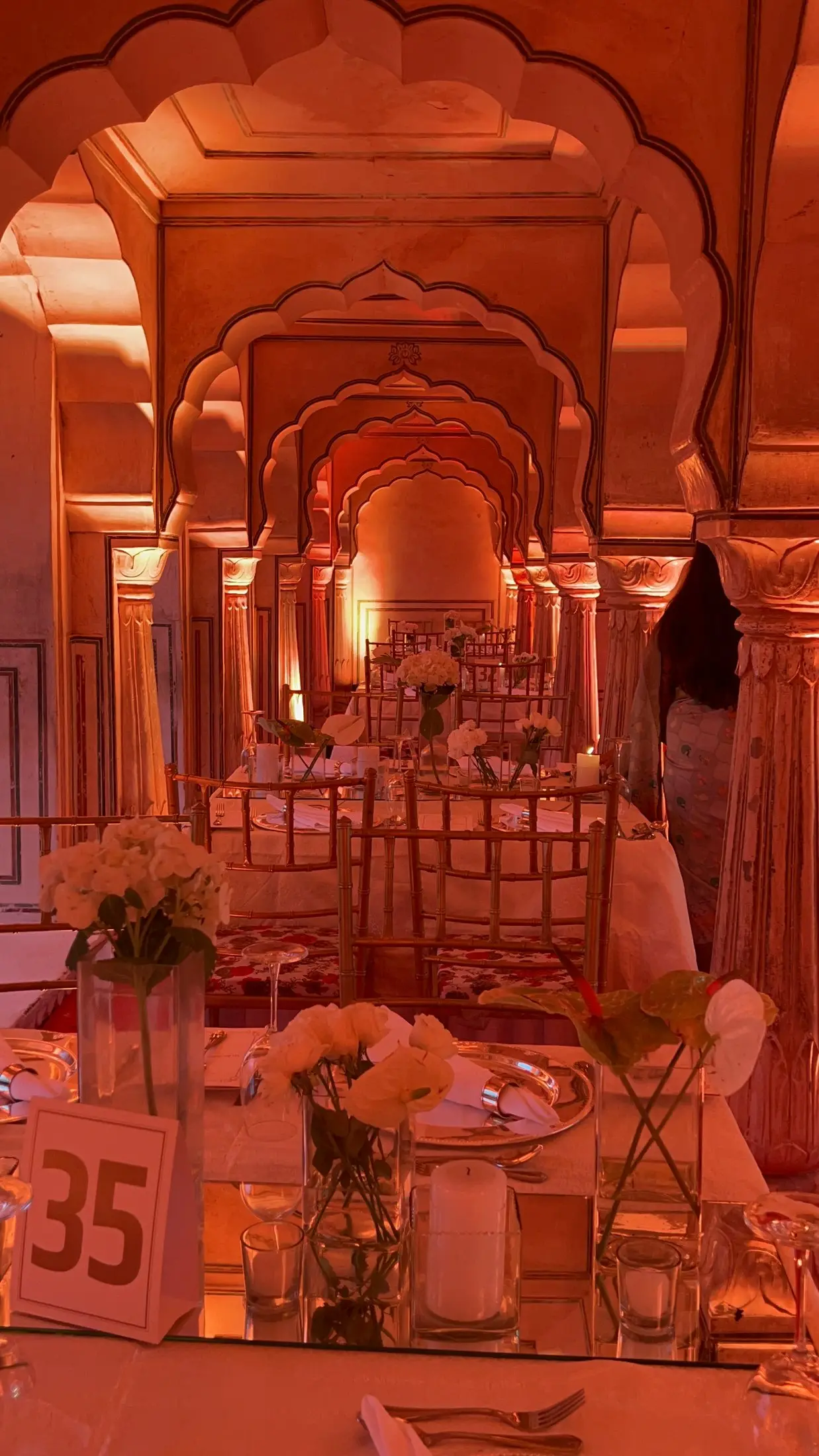 Wedding dinner tables set beneath carved arches lit in warm amber light